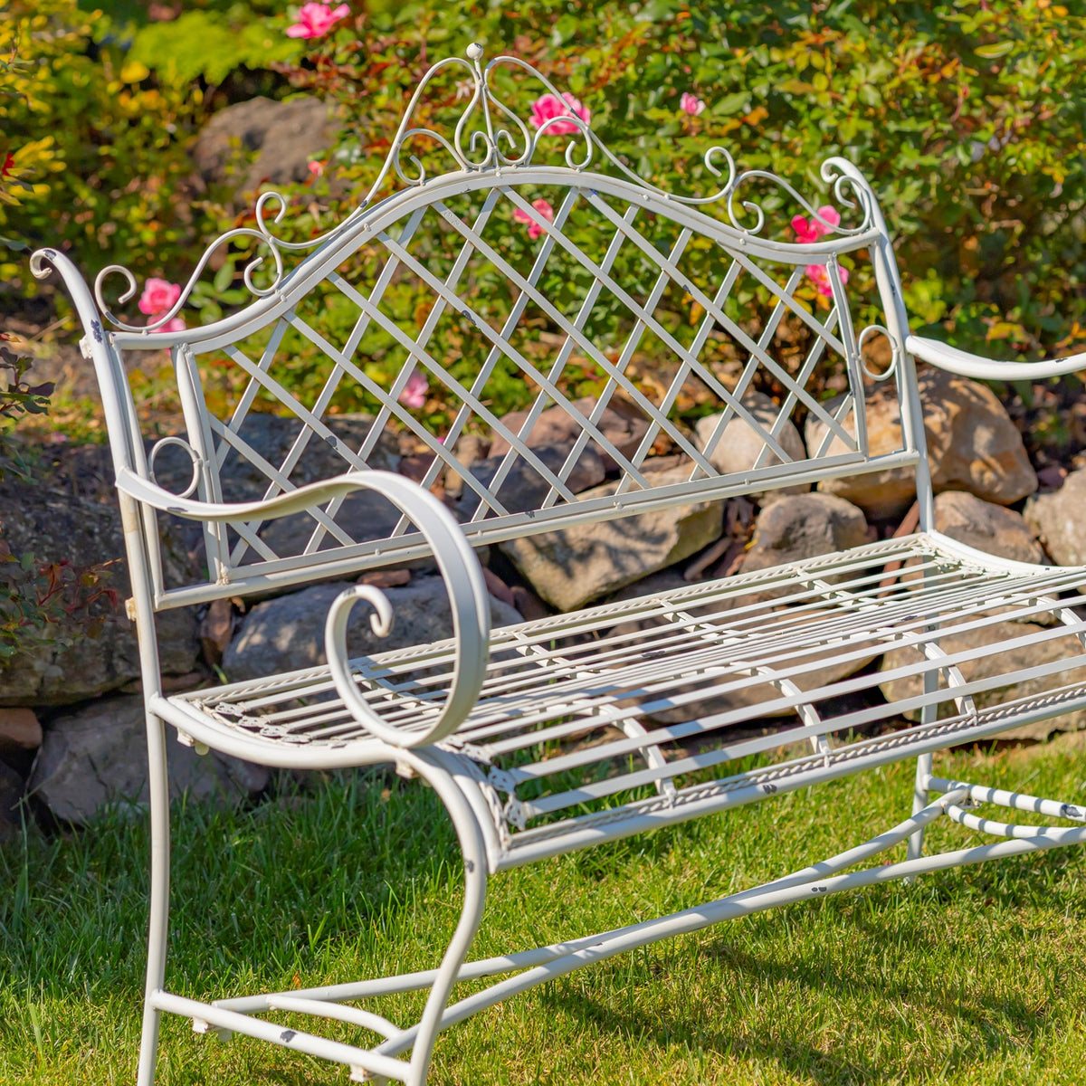 Close angled view of a pale iron bench showing its lattice back and curled armrests