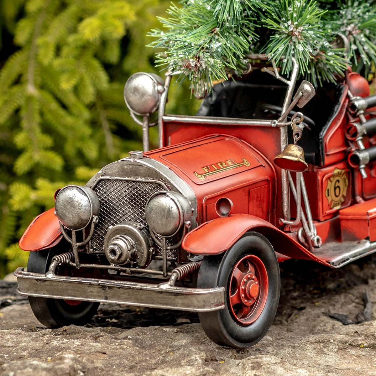 Close-up of the truck’s rounded front, with mesh grille, headlights, red fenders, and evergreen branches above.