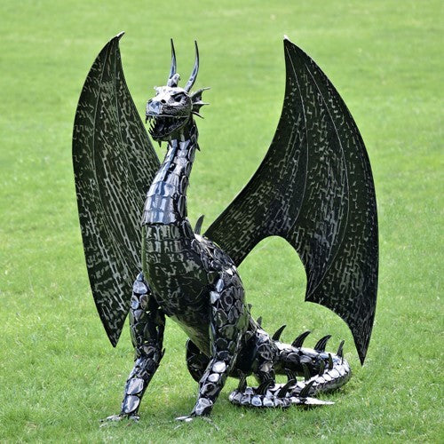 Front view of the dragon statue with both wings spread upright and its tail curled on the grass.