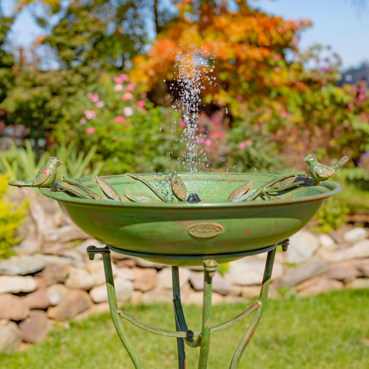 Close view of the birdbath bowl, sculpted birds, and leafy rim as water sprays upward.