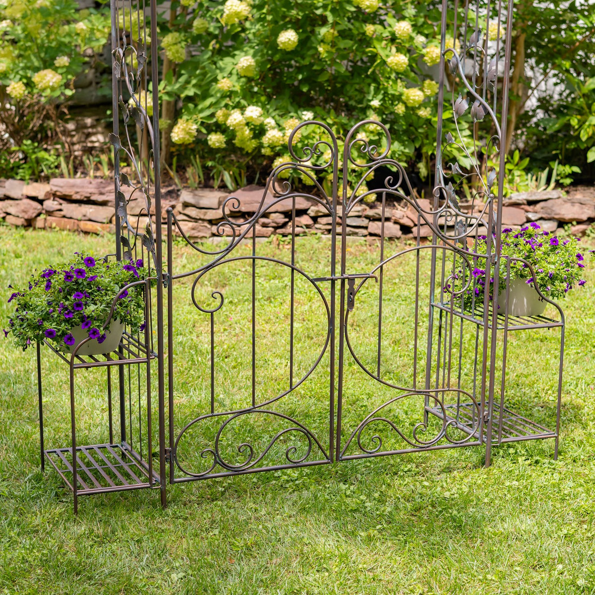 Dark metal garden arch and decorative gate with potted flowers on the side stands.
