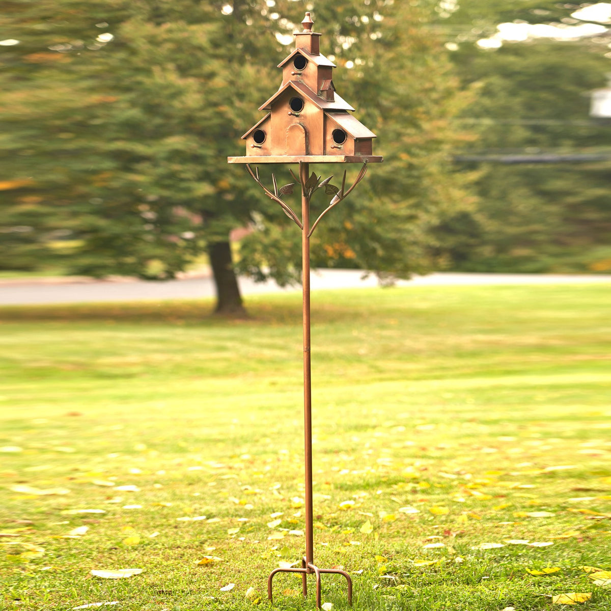 The entire birdhouse stake stands in a lawn, with its tall pole and pronged ground support visible.