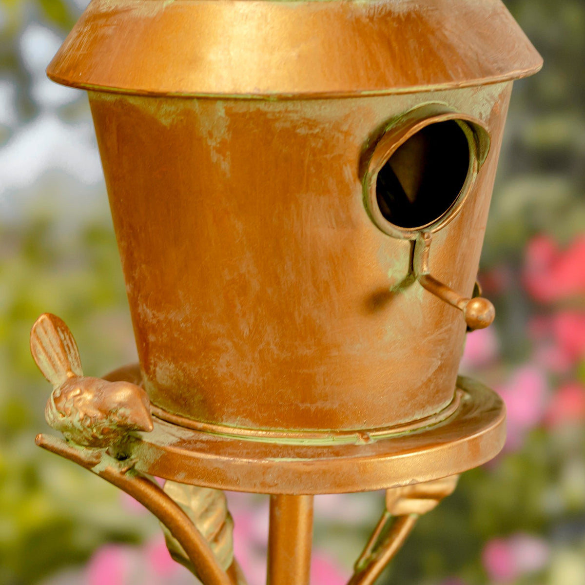 Close-up of the birdhouse entrance, latch and small bird ornament on the copper-colored base.