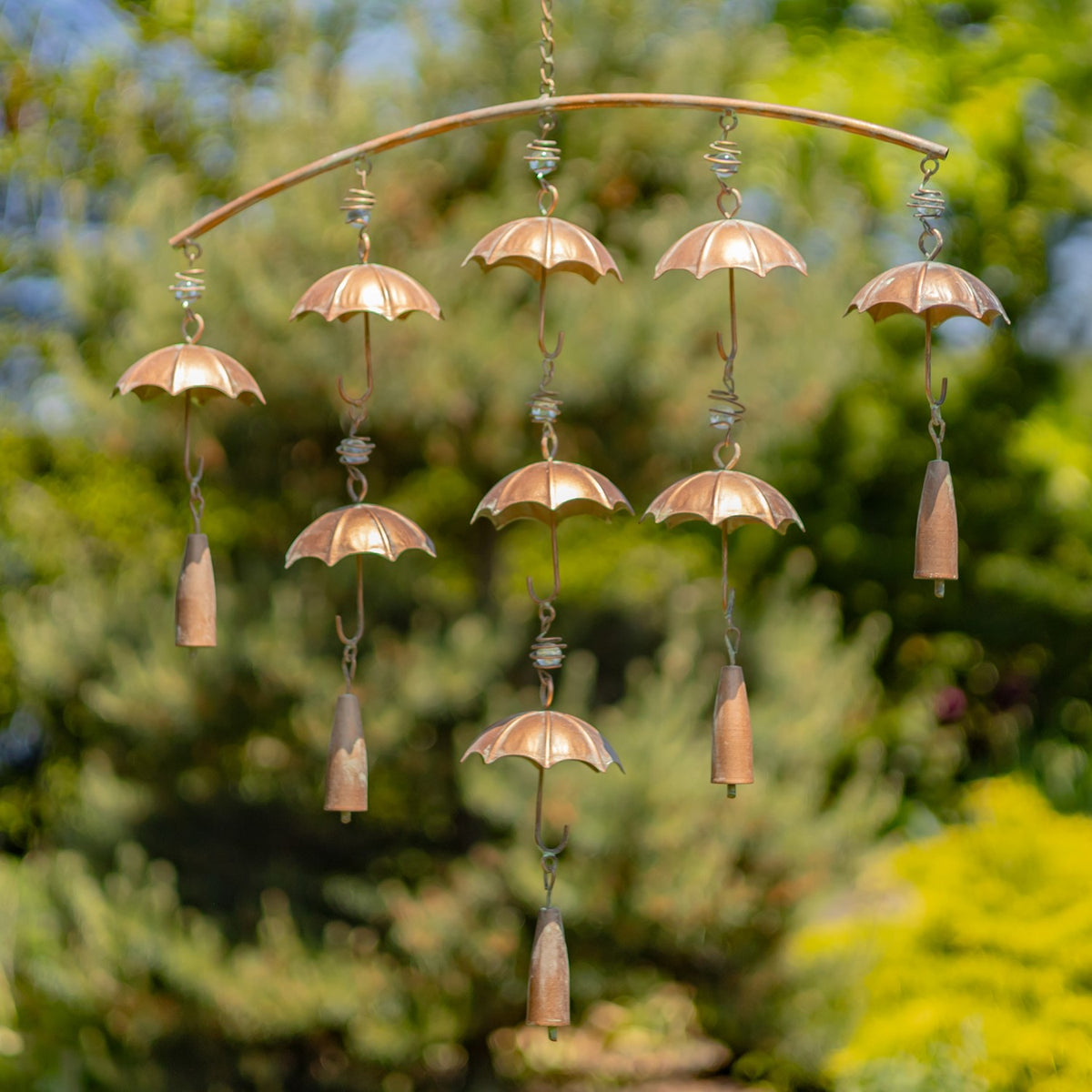 Full umbrella wind chime with bells against a leafy garden backdrop
