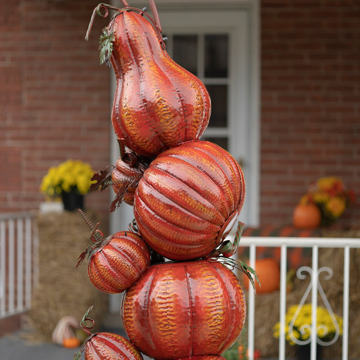 Close-up of ribbed orange pumpkins, a tall gourd, and curling metal leaves on the arch column.