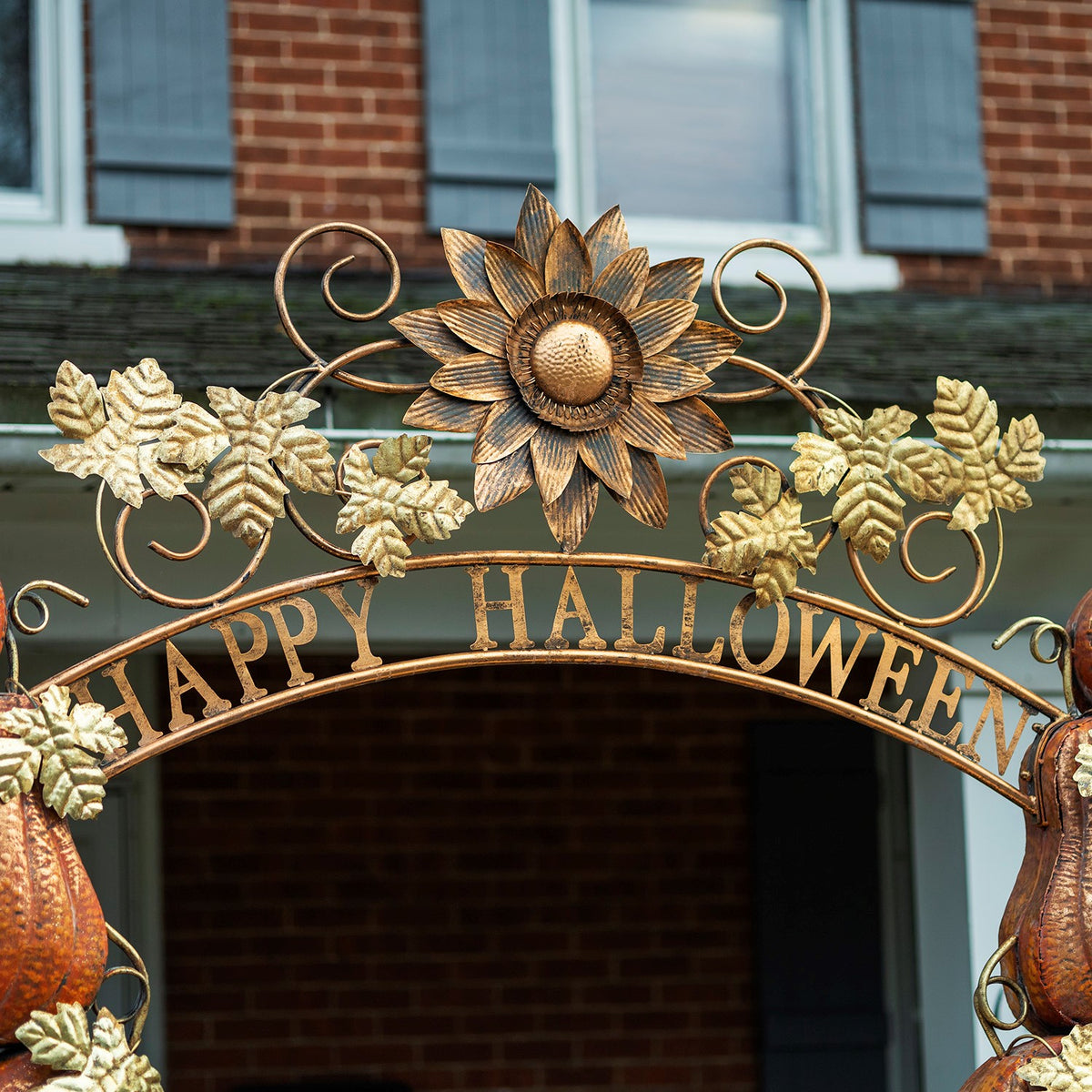 The arch's metal scrollwork, gold-toned leaves, and large sunflower ornament above a curved lettered band.
