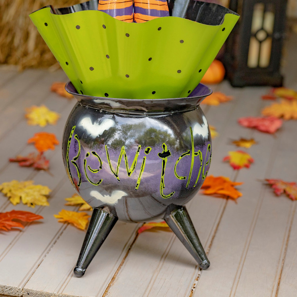 Close view of glossy black cauldron body, green lettering and pointed legs