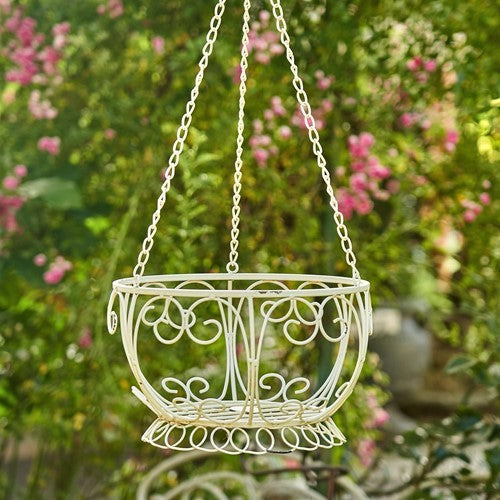 Empty cream-colored hanging iron basket shown against a soft-focus garden backdrop.