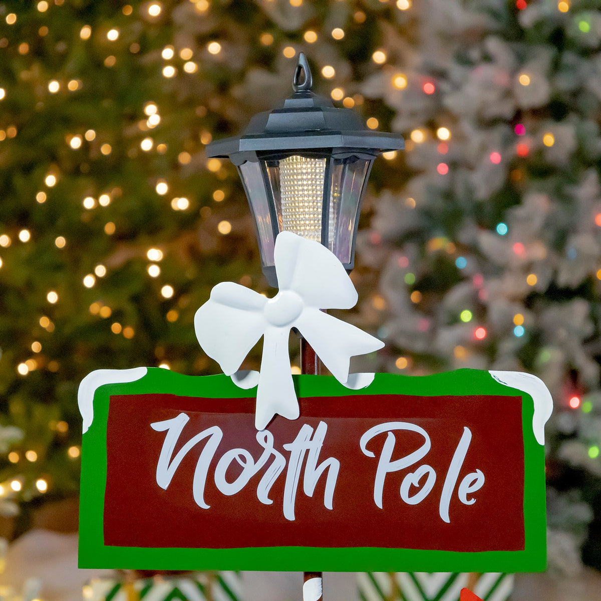 Close view of the glowing lantern, white bow, and upper red-and-green sign against blurred holiday lights.