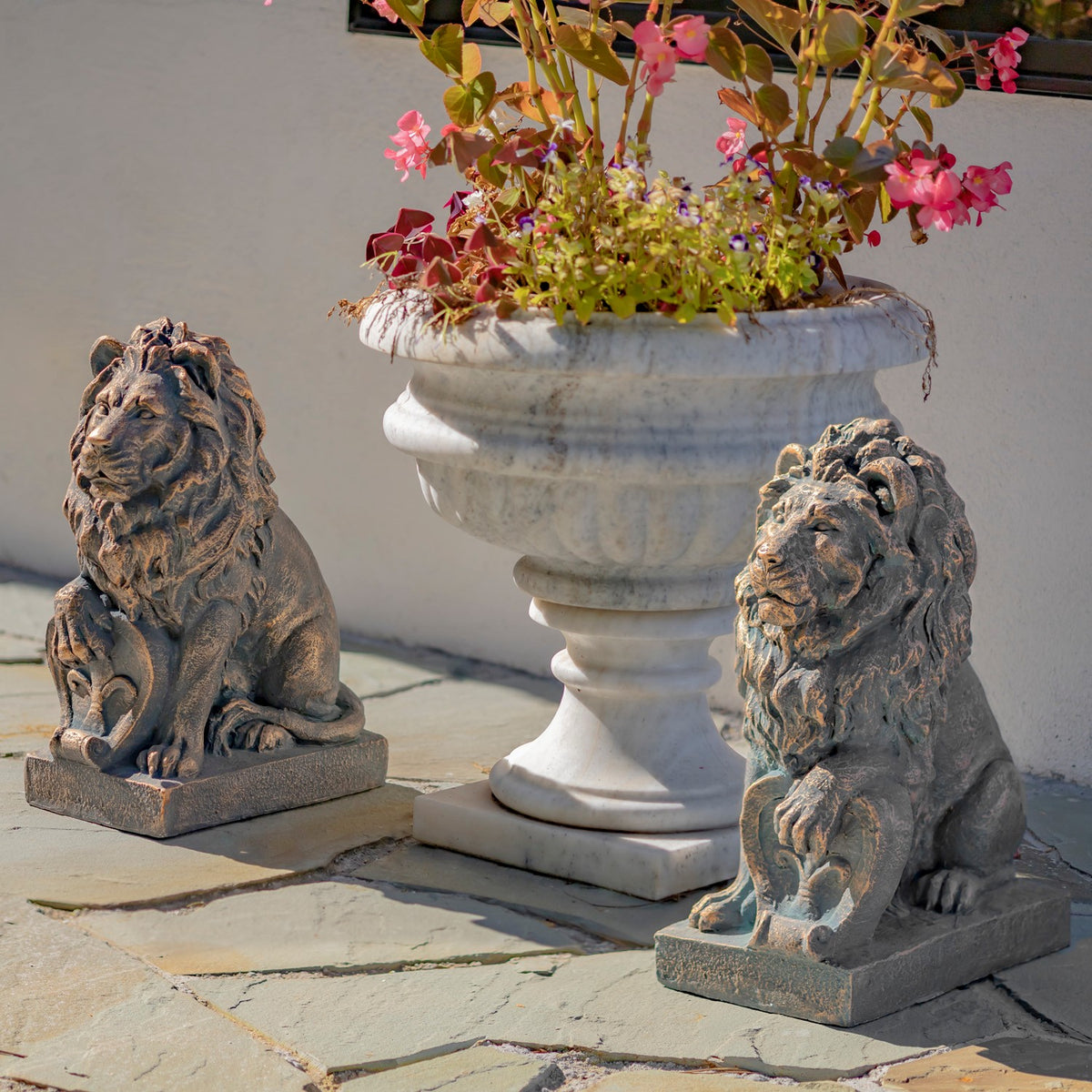 A pair of seated lion statues beside a large white planter filled with flowers.