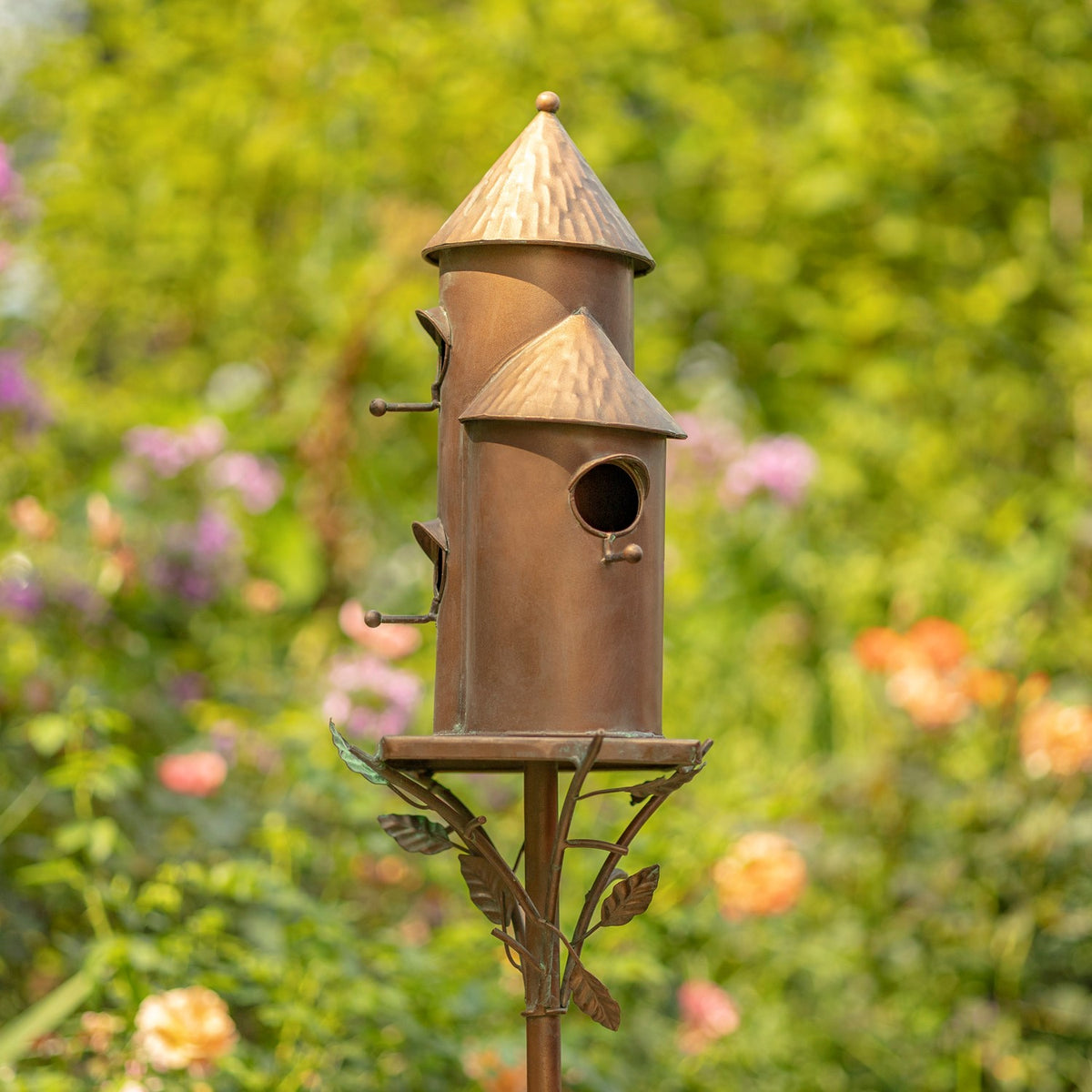 Antique copper birdhouse stake shown from the side among garden flowers