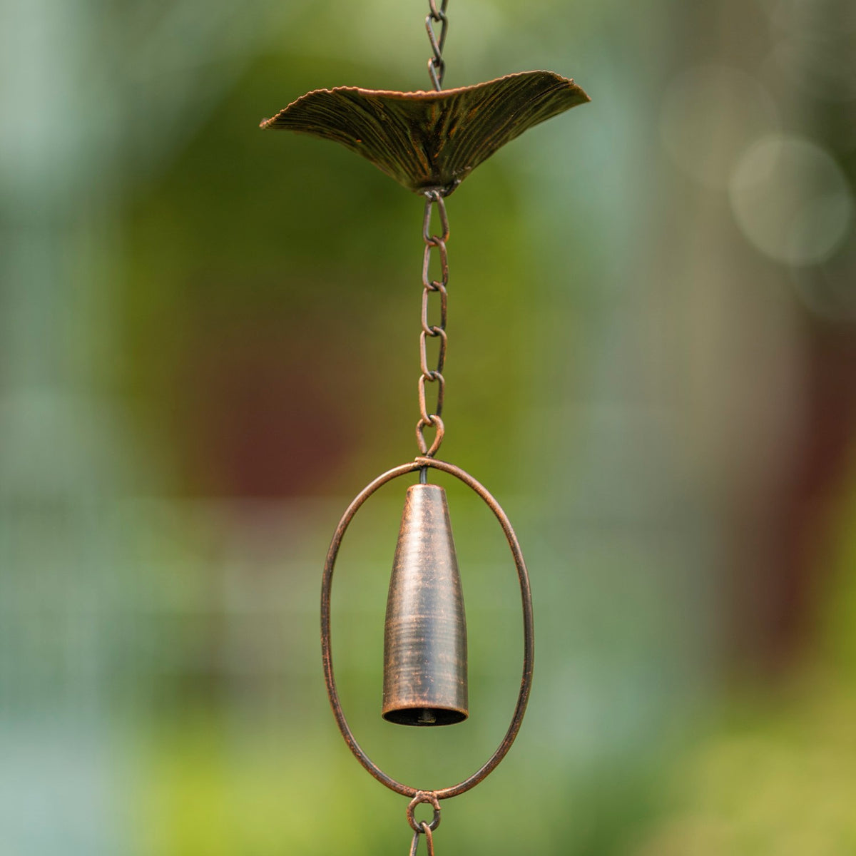 Close-up of a bronze bell suspended in an oval frame beneath a textured mushroom-shaped cup.