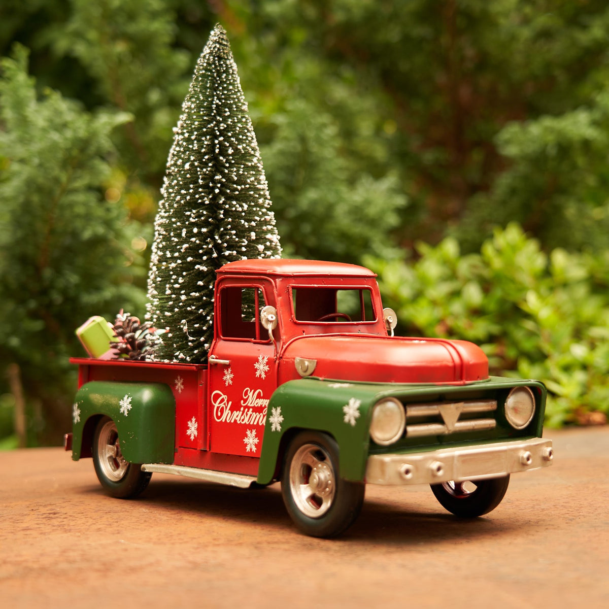 Front three-quarter view of a red and green Christmas truck beside a miniature tree