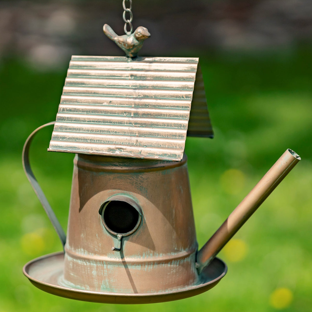 Copper-toned birdhouse with a ridged pitched roof, teapot handle, long spout, and circular entrance.