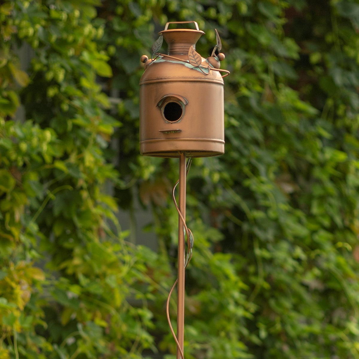 Birdhouse on a slender garden stake, showing its circular opening and curved vine detail.