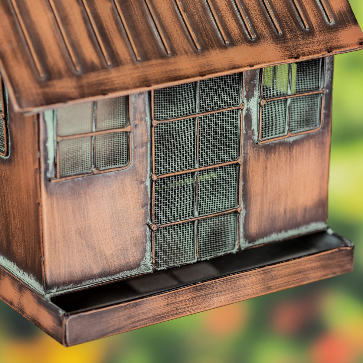 Close view of the feeder’s mesh openings, weathered copper-colored panels, and shallow base tray.