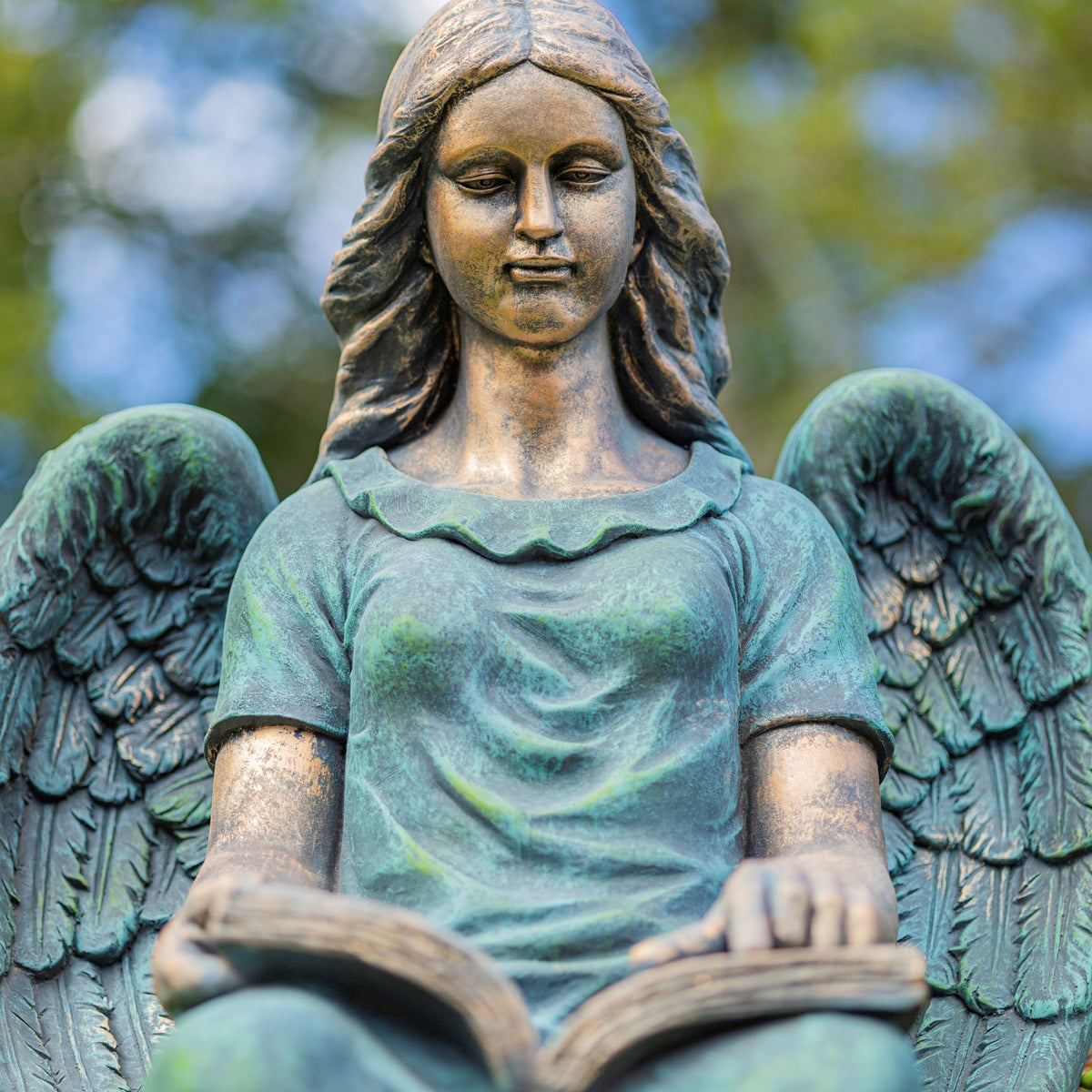 Close view of the angel's face, feathered wings, and hands resting on an open book.