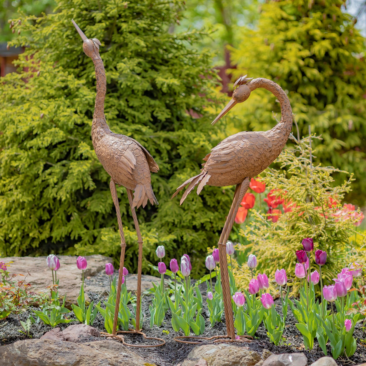 Two rustic crane figures seen from behind among flowers in a garden