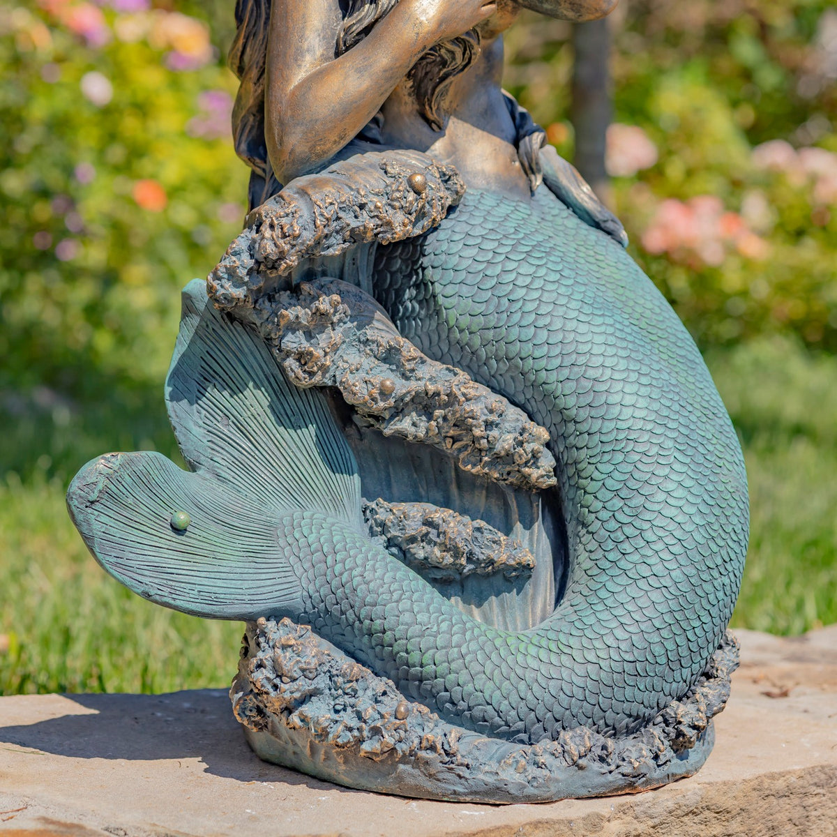 Close-up of the mermaid’s curled scaled tail and the textured rock base beneath it.