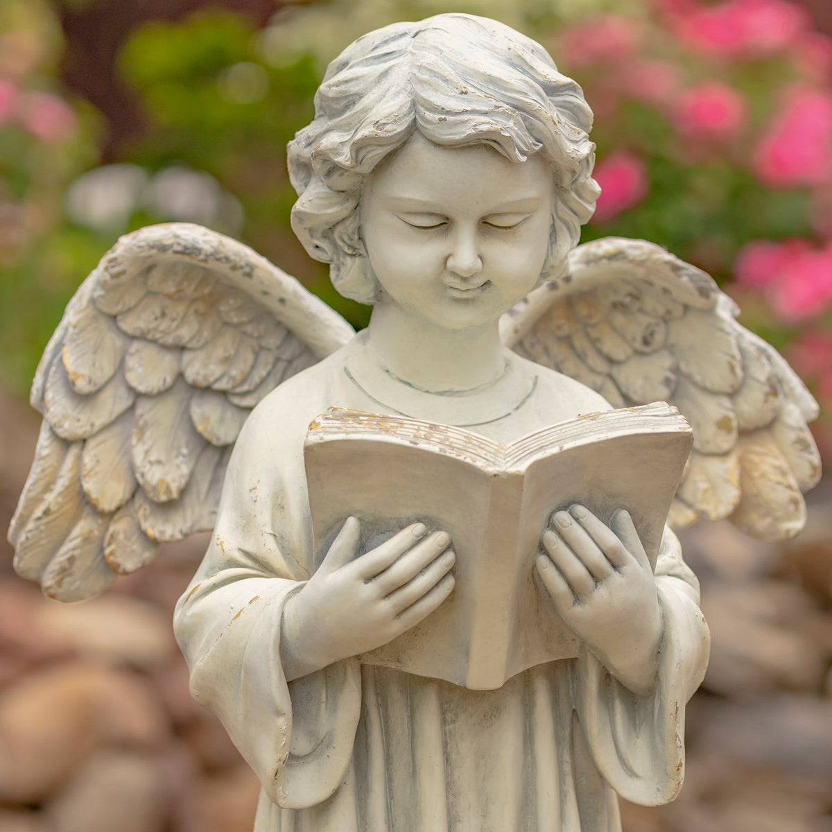Close-up of the angel’s serene face and hands holding an open book, with feathered wings behind.