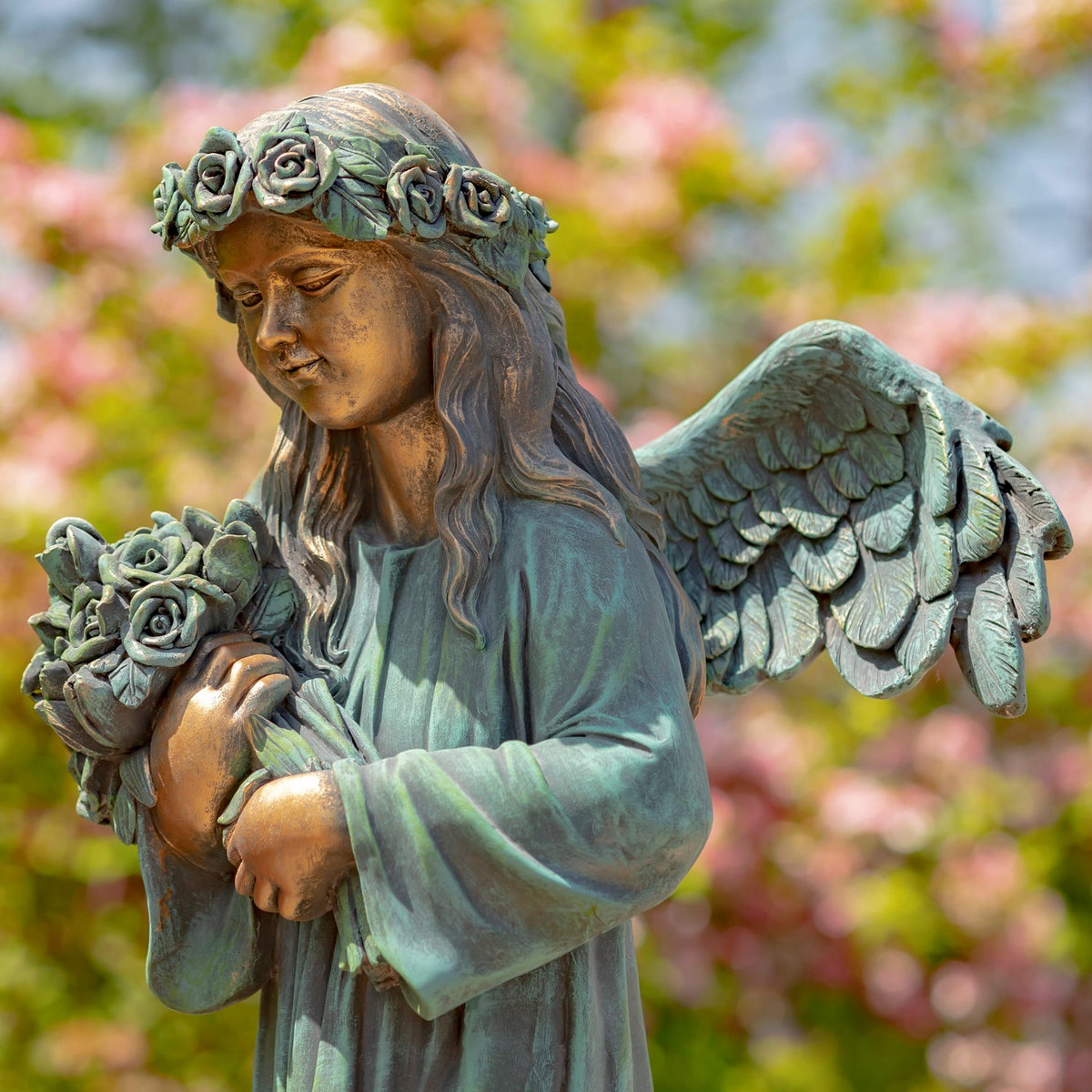 Close view of the statue holding roses, with her wing and layered robe visible against flowering trees.
