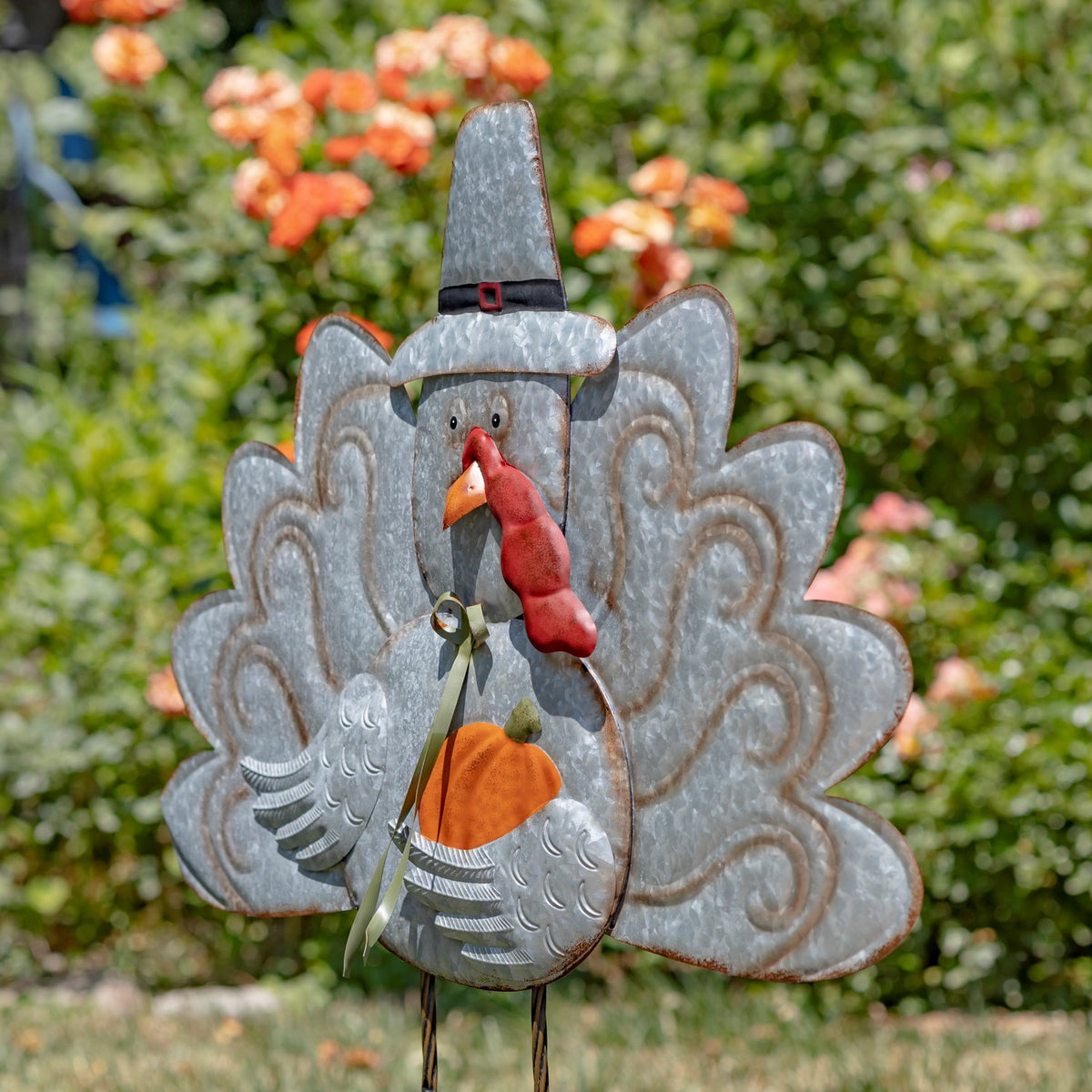Angled view of the turkey stake standing on two narrow metal legs in a flower garden.