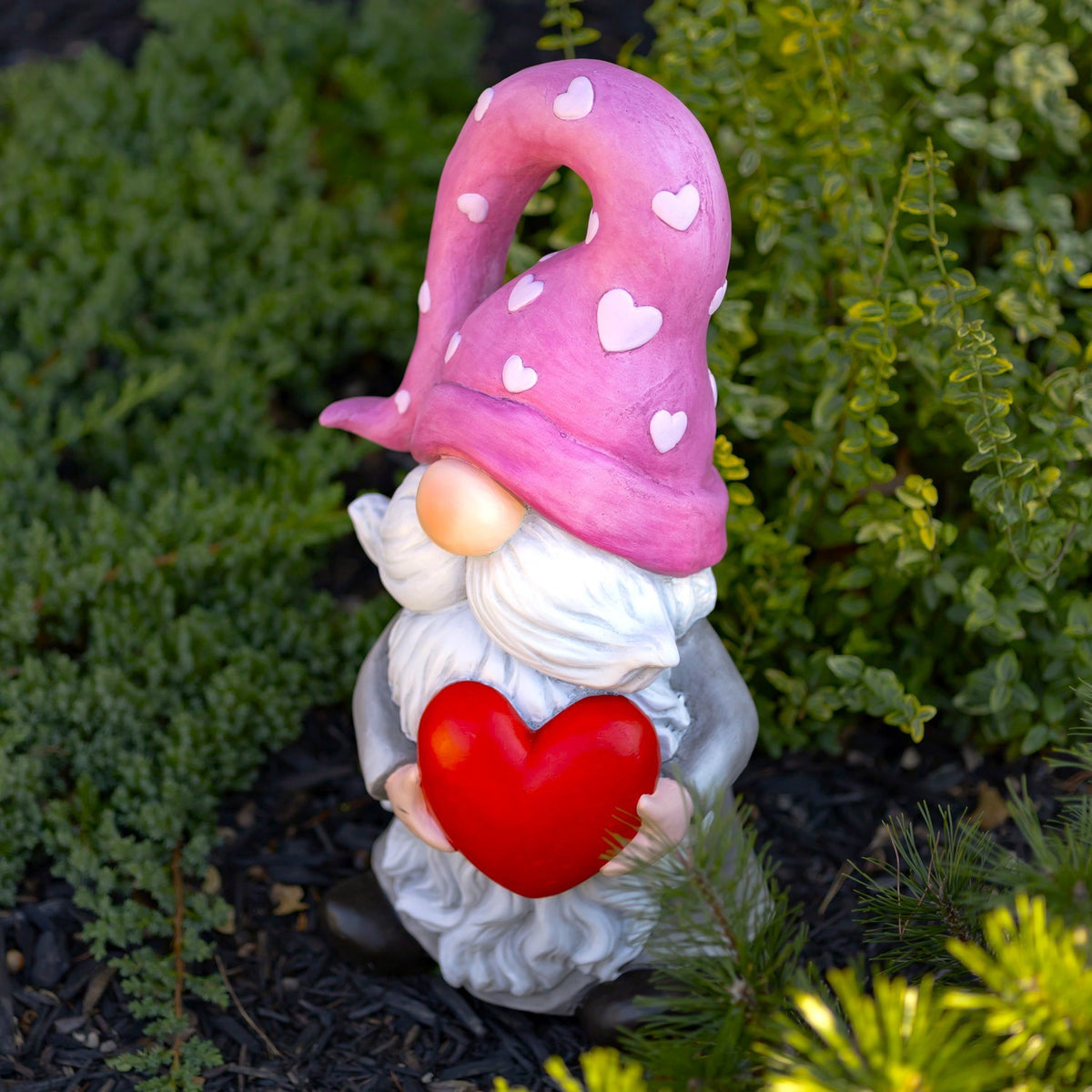 Angled front view of a heart-holding gnome in a garden bed