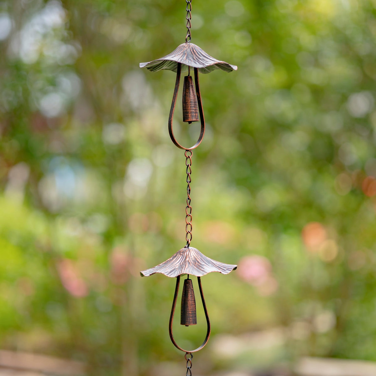 Two antique bronze mushroom bells on a rain chain in a garden setting