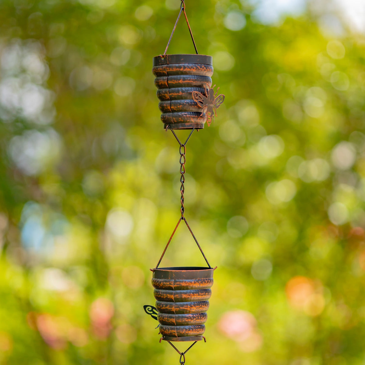 Two antique bronze bucket hive cups linked on a rain chain outdoors