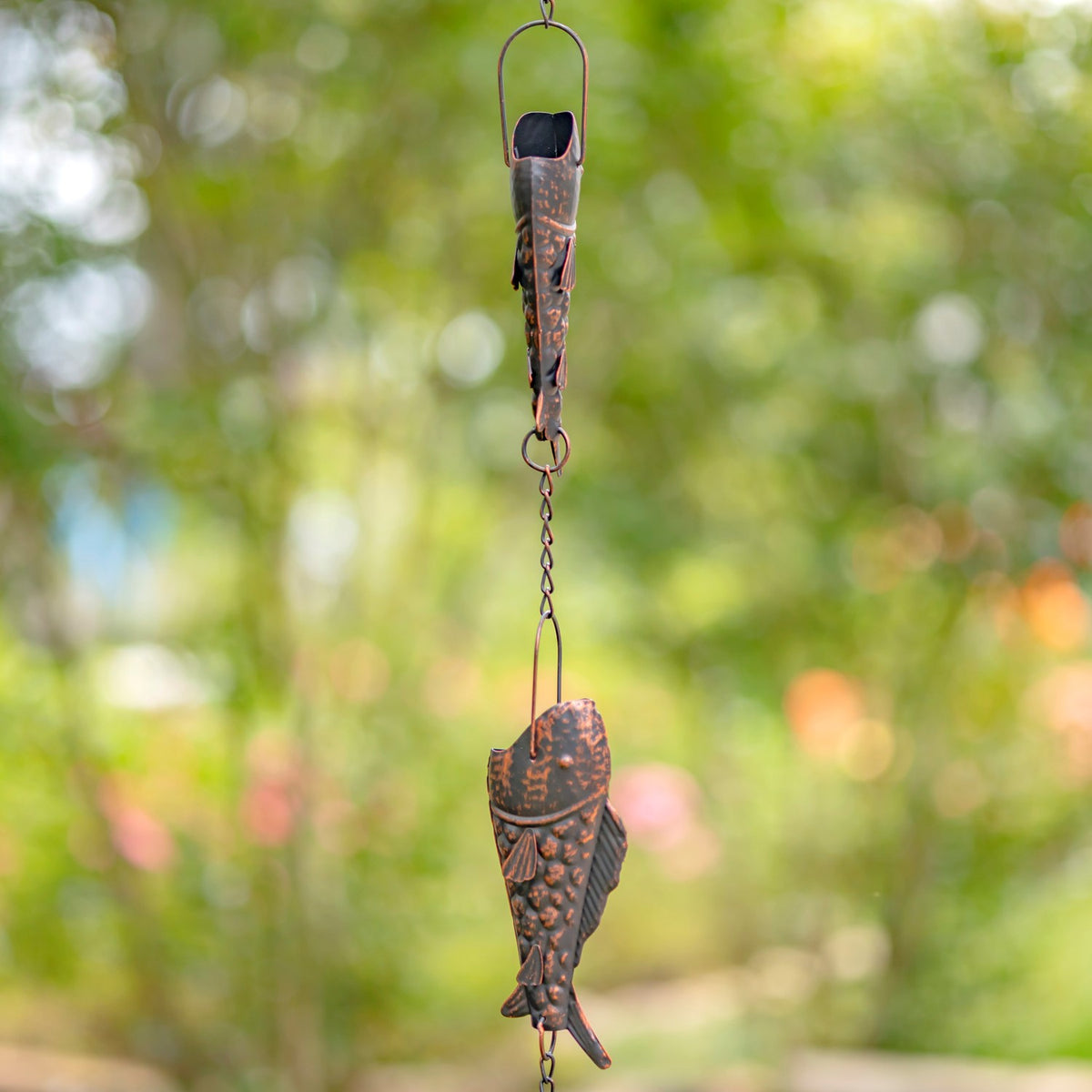 Side view of antique bronze trout pieces linked on a garden rain chain