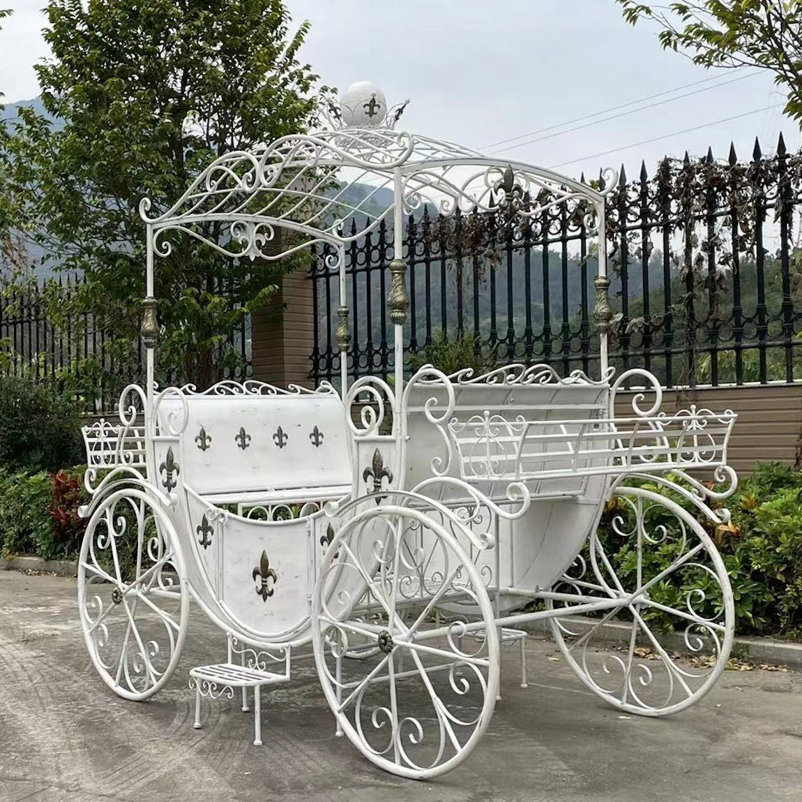White iron carriage with side planters and large decorative wheels on a paved path