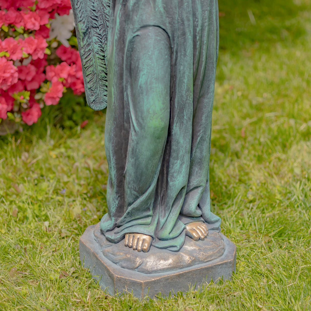 Close view of the statue's draped robe, bare feet, and sculpted base on the grass.