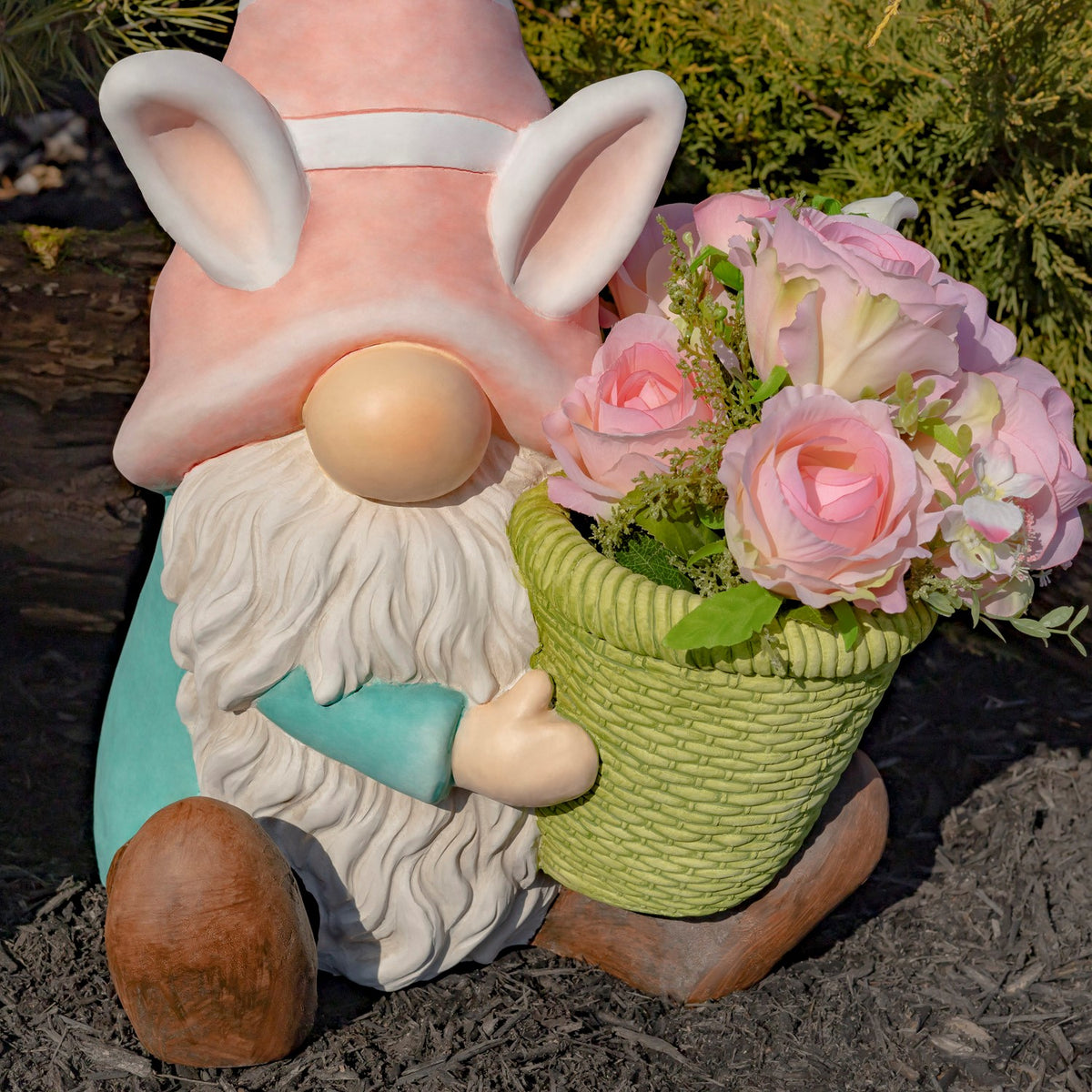 A pink-hatted gnome with a white beard sits beside a green planter of pink roses.