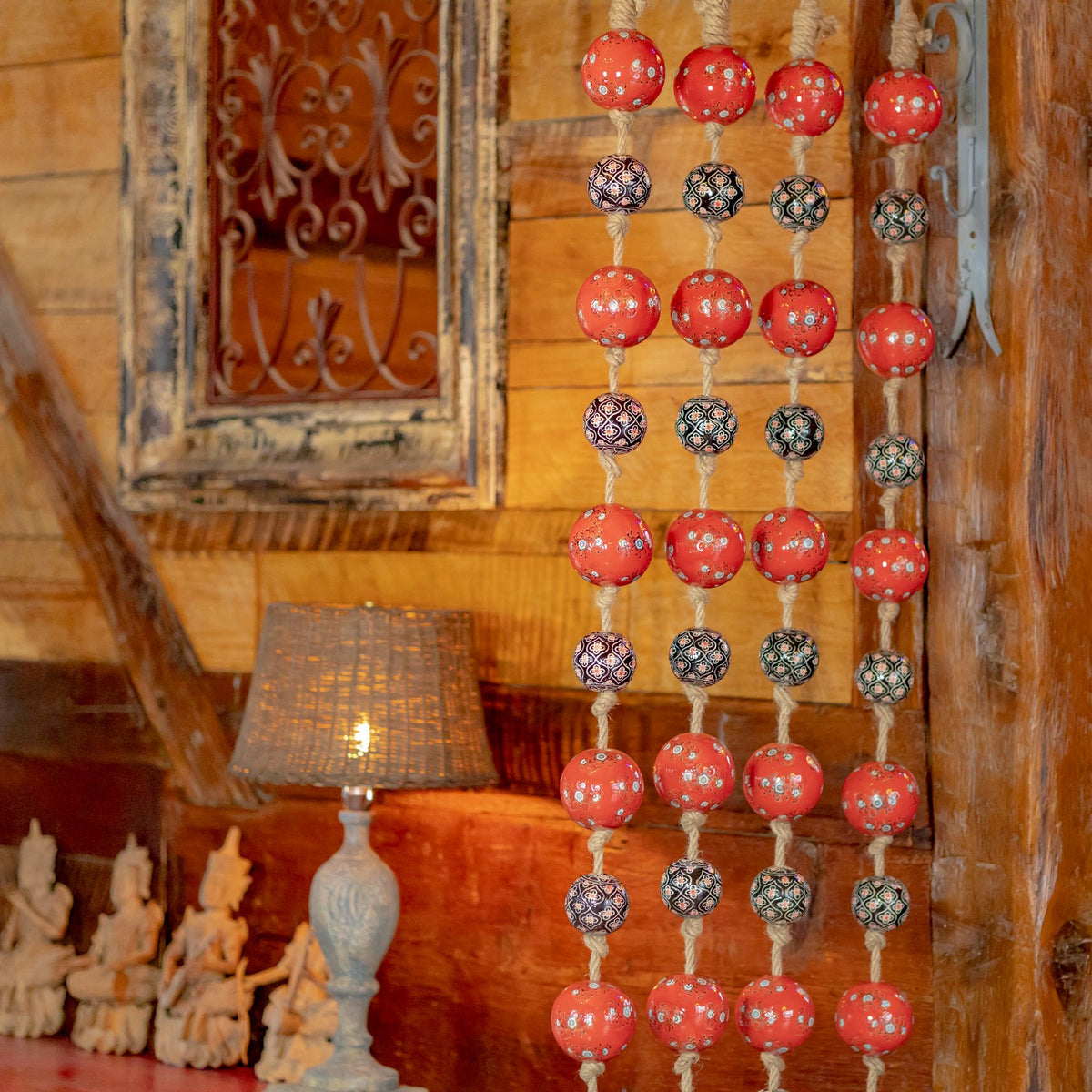 Four hanging strands of alternating red and patterned balls against a warm wood-paneled wall.