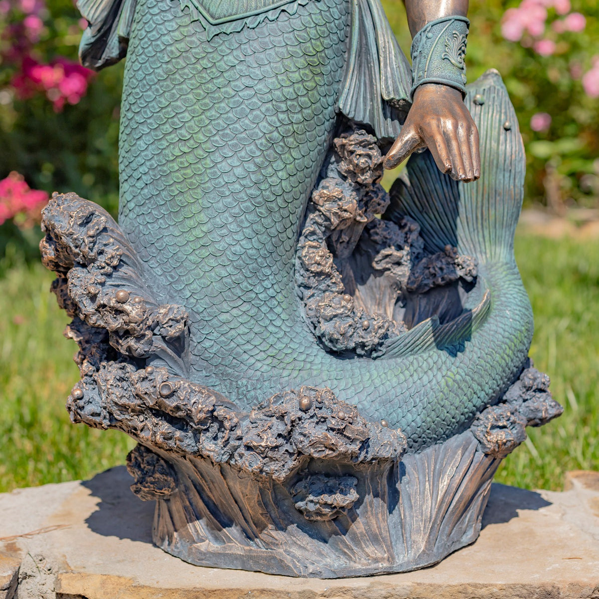 Close-up of the scaled tail, fin, rocky base and the statue’s hand.