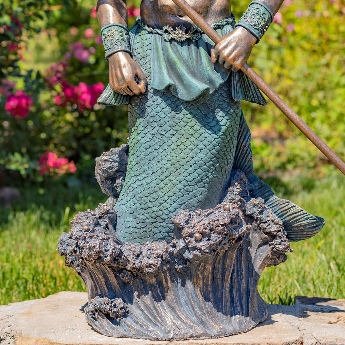 Close view of the statue’s scaled turquoise tail and textured wave base, with the trident crossing above.
