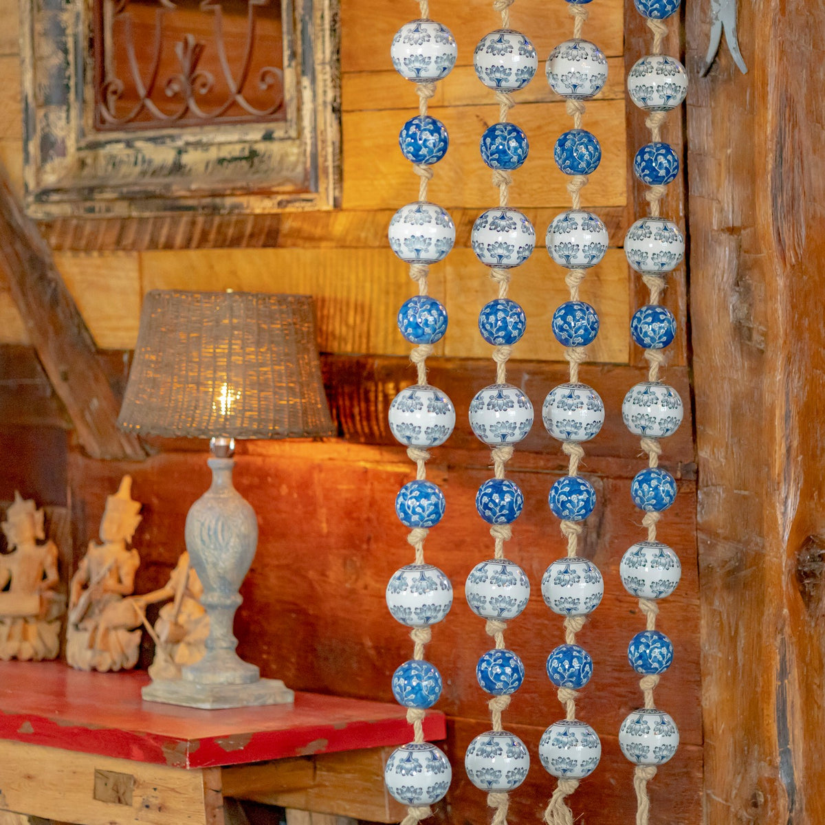 Four long patterned ball garlands hang beside a lit table lamp in a warm, rustic interior.