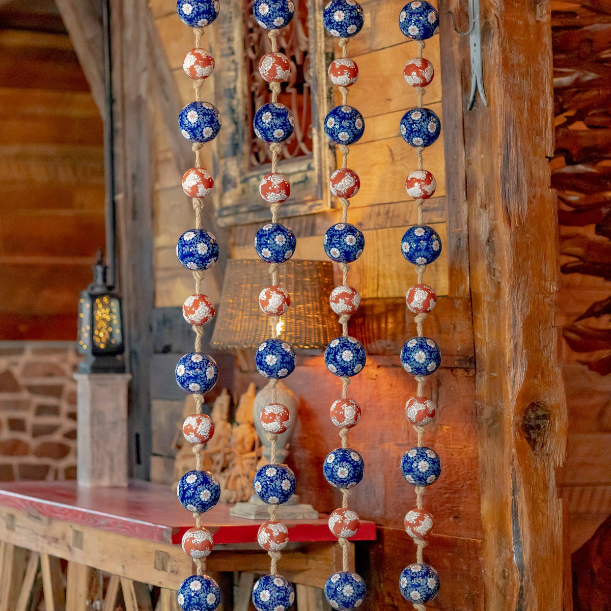 Four hanging strands of patterned blue and burnt-orange balls shown against a wooden interior.