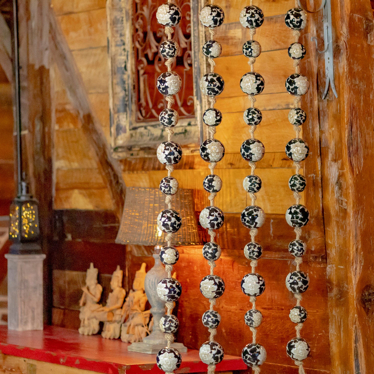 Four patterned ball strands hang against a wooden wall above a red-topped table.