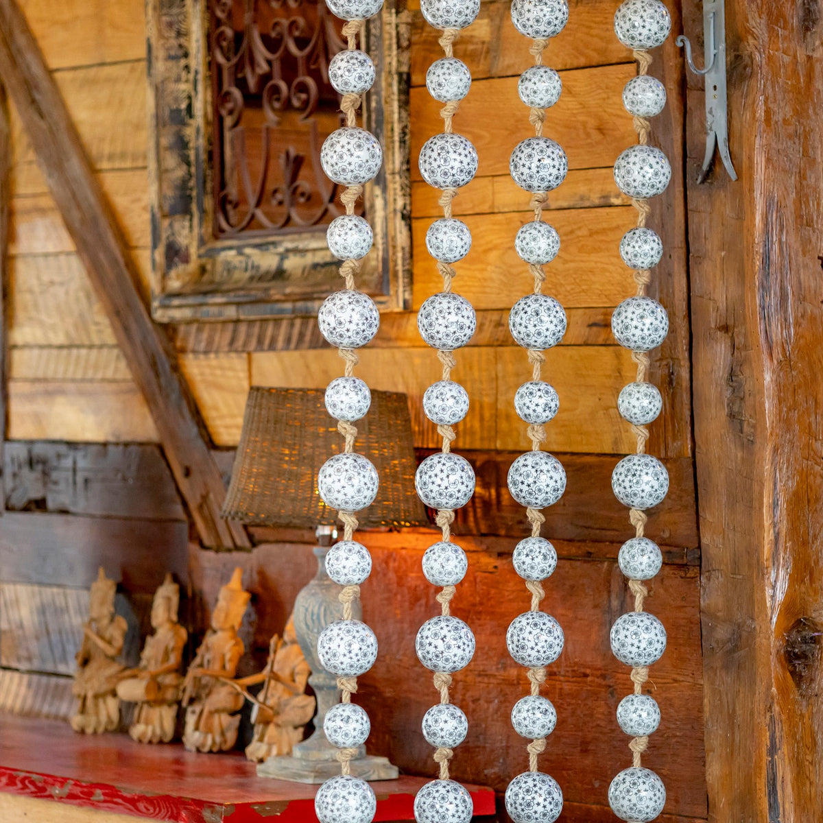 Four vertical strands of black-and-gray patterned white balls hang above a rustic red-topped table.