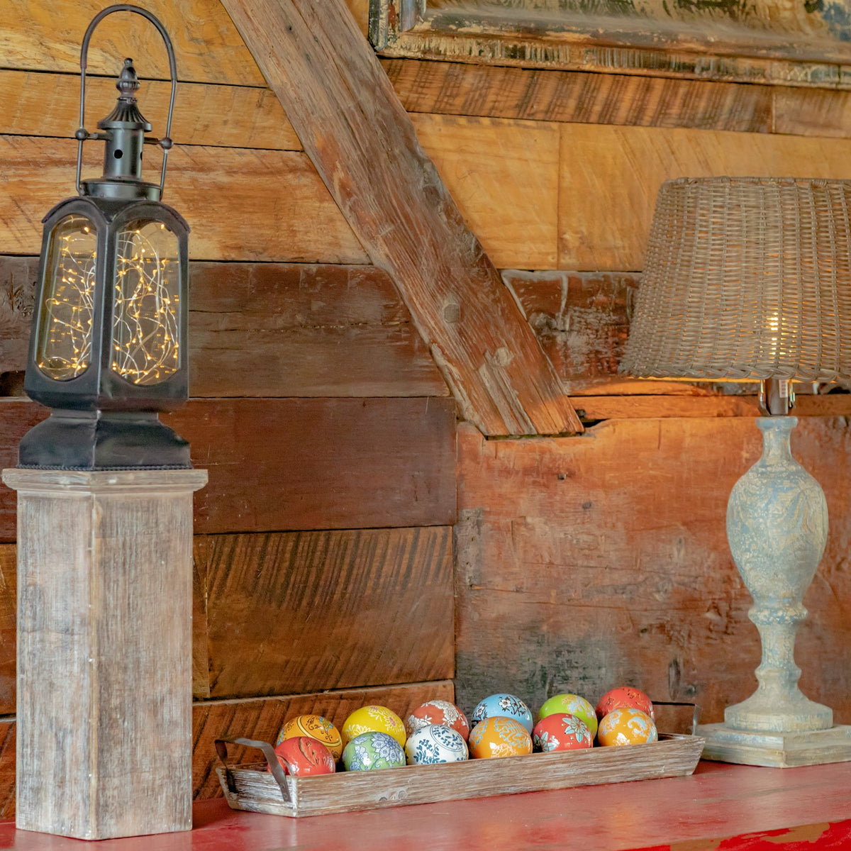 A shallow tray of colorful patterned balls rests on a red tabletop beneath rustic wooden walls.