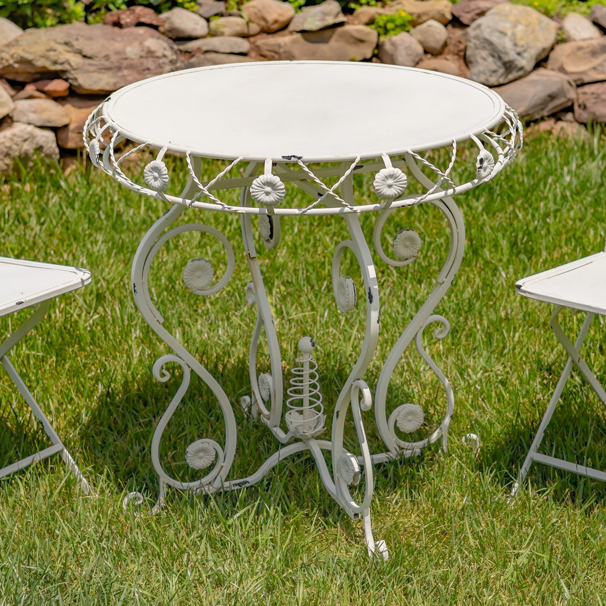 Close view of an antique white bistro table with floral metal accents on grass
