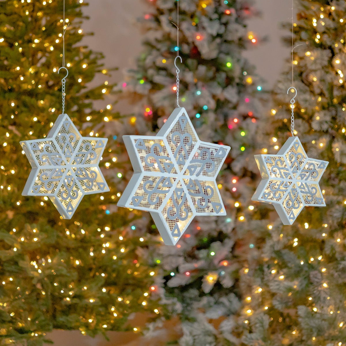 Three hanging illuminated snowflakes against a colorful holiday light display