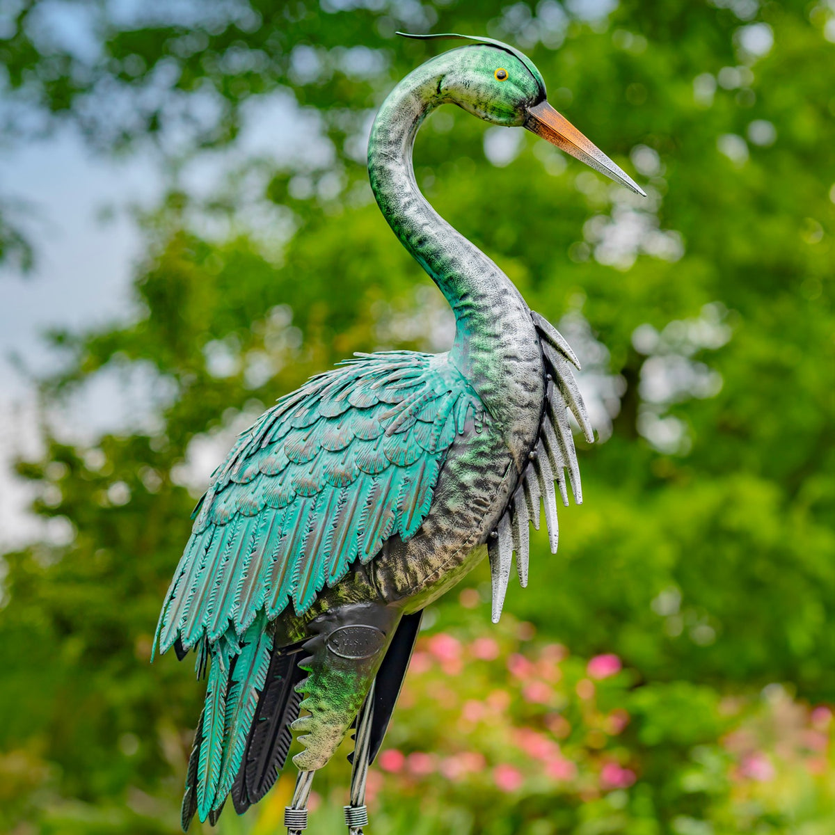 Close view of a teal heron sculpture with folded wings, a pointed beak, and slender metal legs.