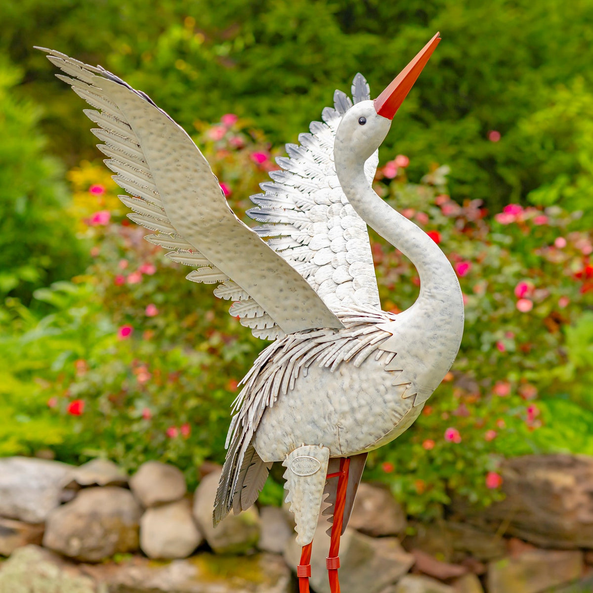 A white heron statue raises one broad, feathered wing beside a stone garden border.