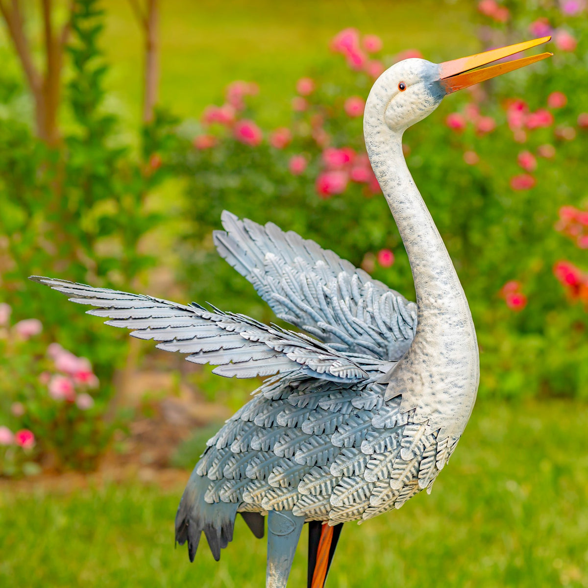 Blue-and-white egret figurine with wings outstretched in a garden