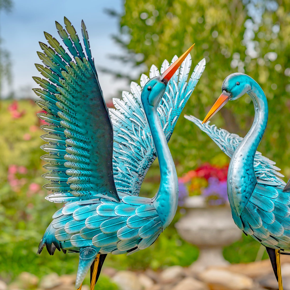 Two blue-green crane figurines with raised wings viewed close-up outdoors