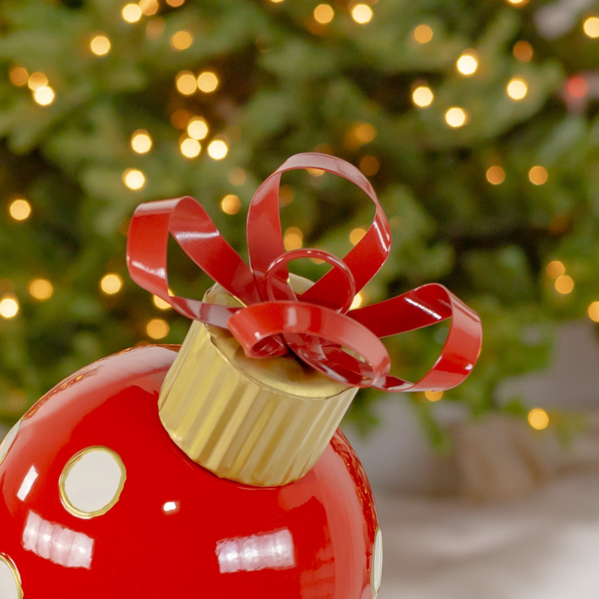 Red curled bow and ridged gold cap above the ornament, with part of its dotted red surface visible.