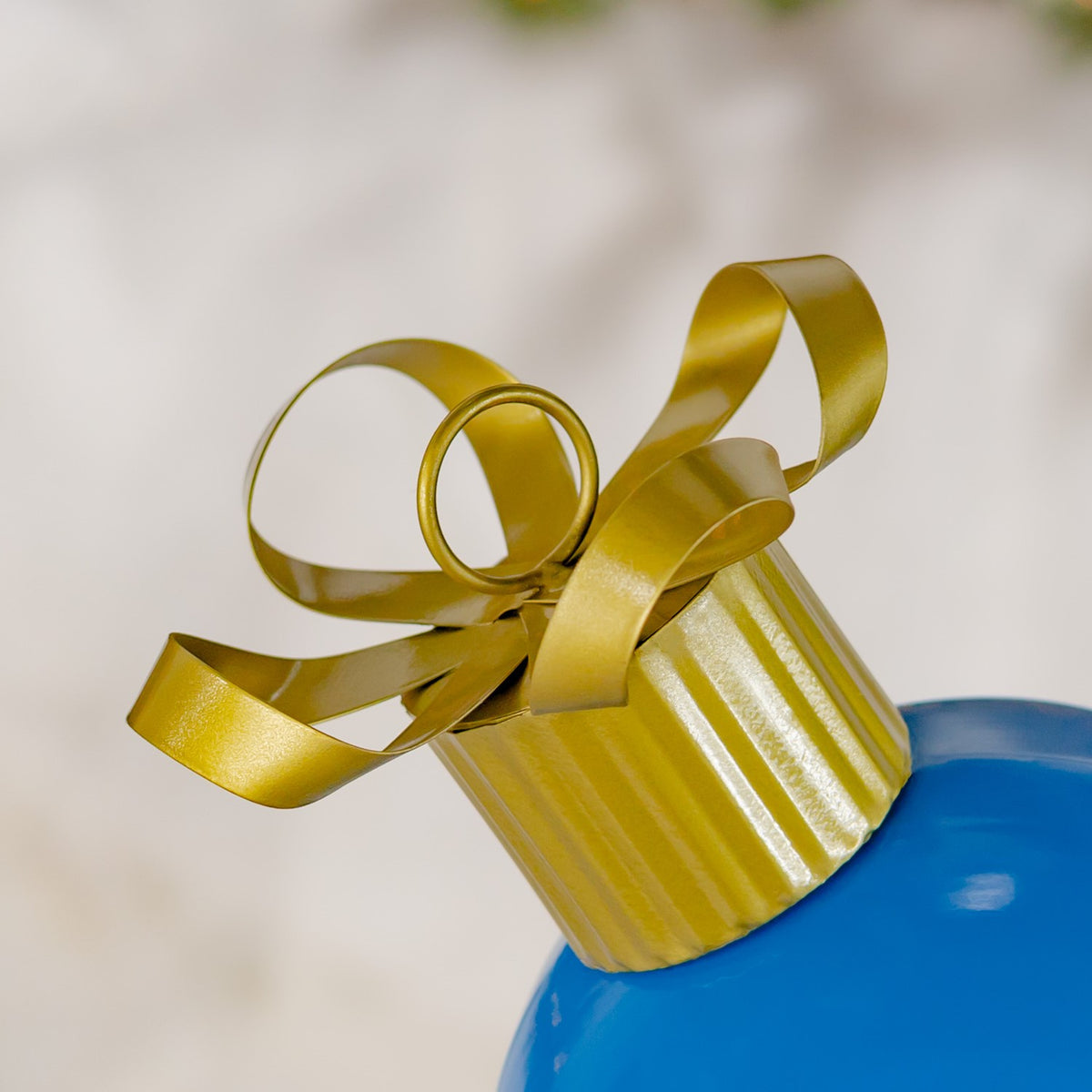 Close-up of the ornament’s gold ribbon loops and ribbed cap against a pale background