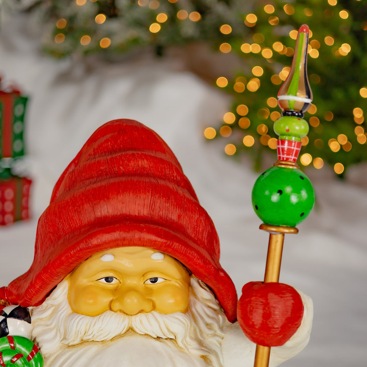 Close-up of a gnome’s face and red hat beside a raised staff with green and red ornaments.
